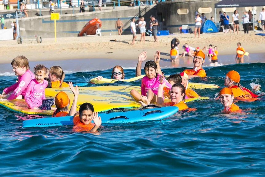 Group of children and an instructor swimming in the ocean with floatation devices.