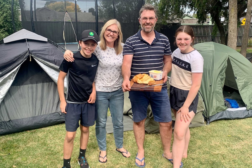 A mother and father stand with their teenage son and daughter holding damper in front of a tent