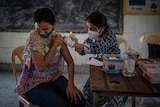 A woman reacts as a health worker inoculates her during a vaccination drive against coronavirus