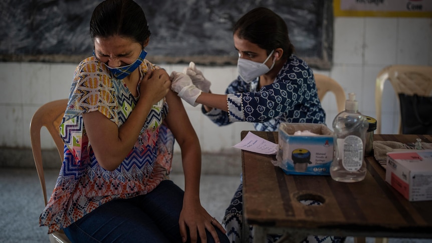 A woman reacts as a health worker inoculates her during a vaccination drive against coronavirus