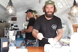 Two people making coffee in a little caravan
