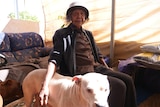 An Indigenous woman pats a dog on a couch.