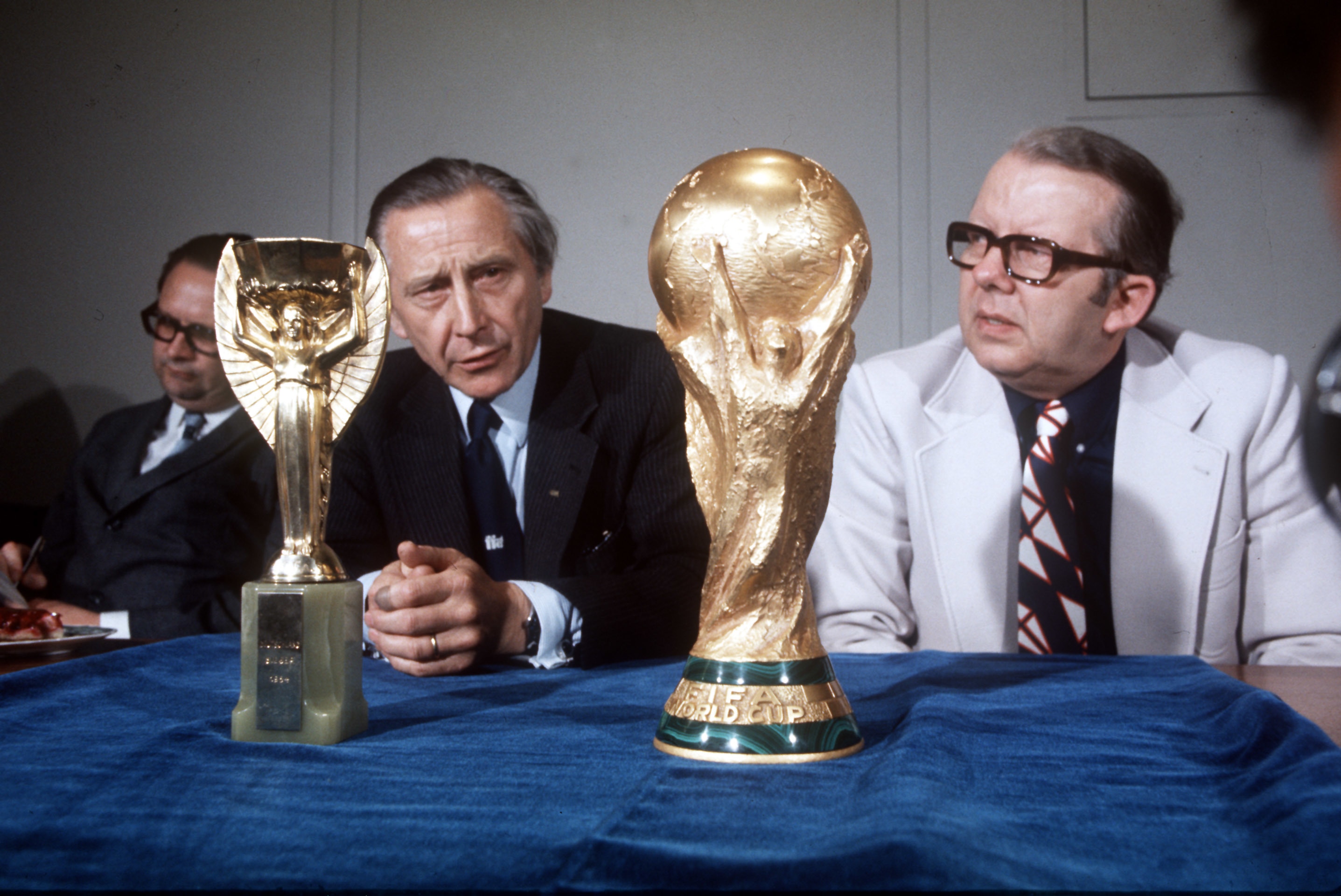 Two men sitting at a table with two trophies on it