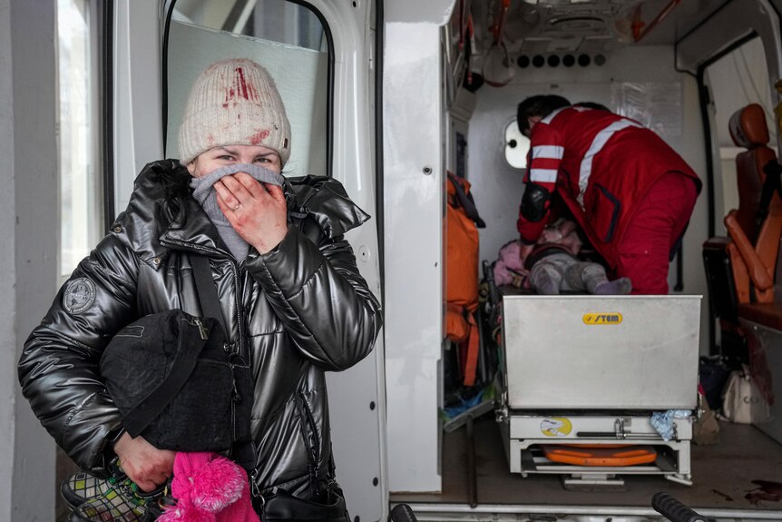 A woman stands next to an ambulance while inside the vehicle a paramedic tries to revive a little girl. 
