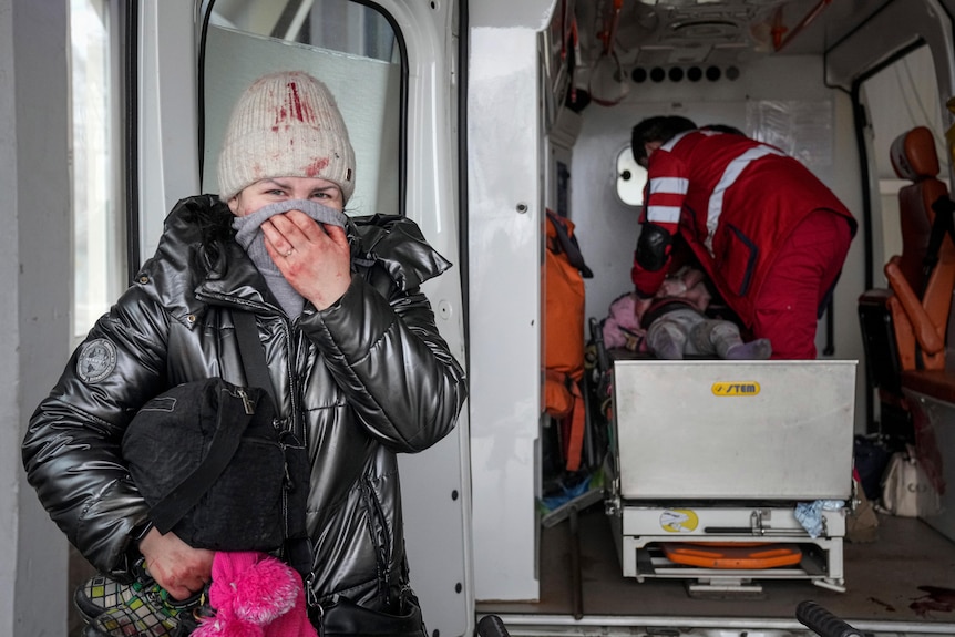 A woman stands next to an ambulance while inside the vehicle a paramedic tries to revive a little girl. 