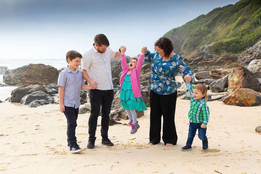 A family photo on the beach, holding up a child in a pink jumper and green dress