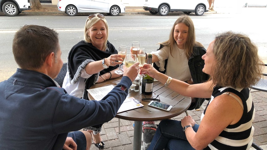 Four people smile and laugh as they chink glasses at a pub in Adelaide.