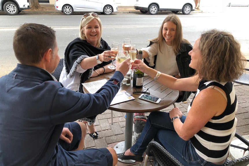 Four people smile and laugh as they chink glasses at a pub in Adelaide.