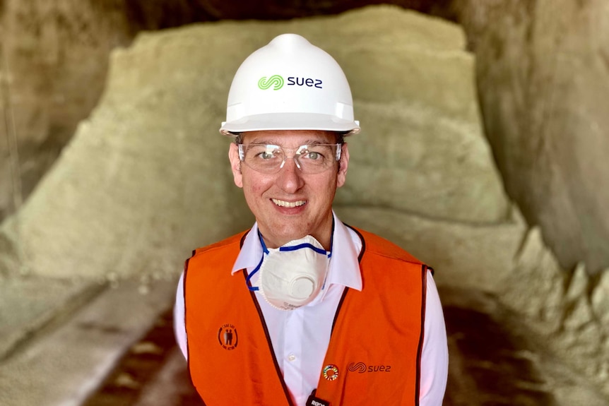 A man in a high vis vest and hard hat stands in front of a pile of sand