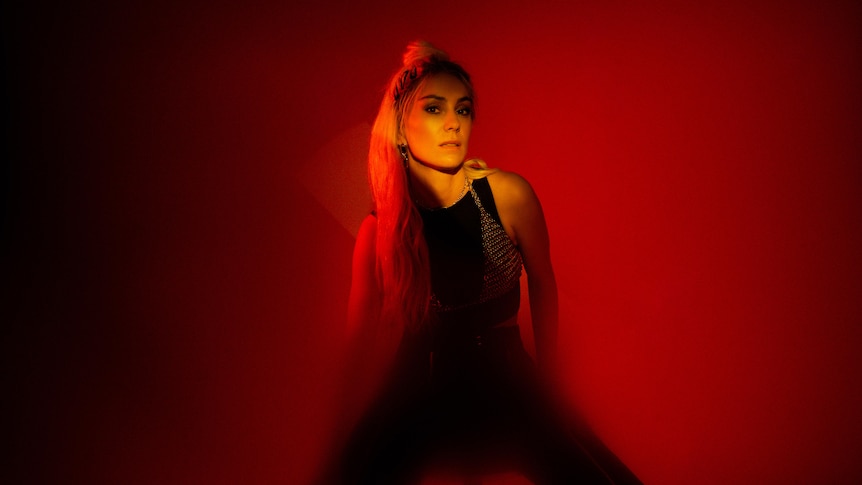 A 2022 press shot of Amy Shark bathed in red light with a blonde ponytail