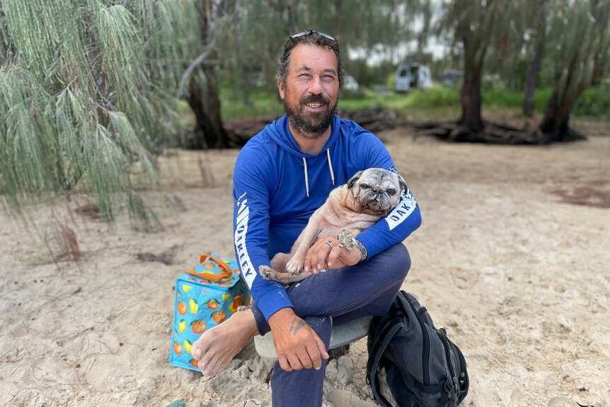 a man sitting on the sand with his dog in his lap