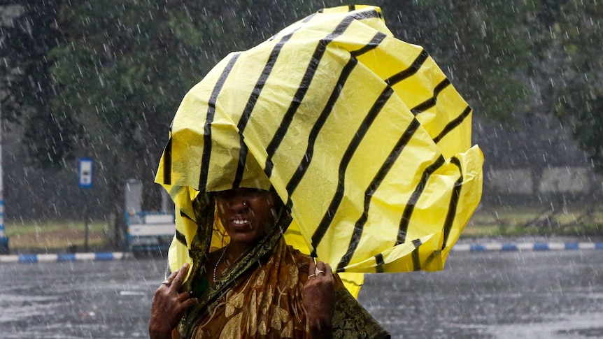 A woman whose saree is drenched in the rain covers her head with a yellow and black plastic bag to protect against the rain.