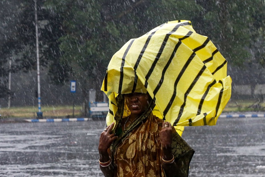 A woman whose saree is drenched in the rain covers her head with a yellow and black plastic bag to protect against the rain.