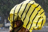A woman whose saree is drenched in the rain covers her head with a yellow and black plastic bag to protect against the rain.