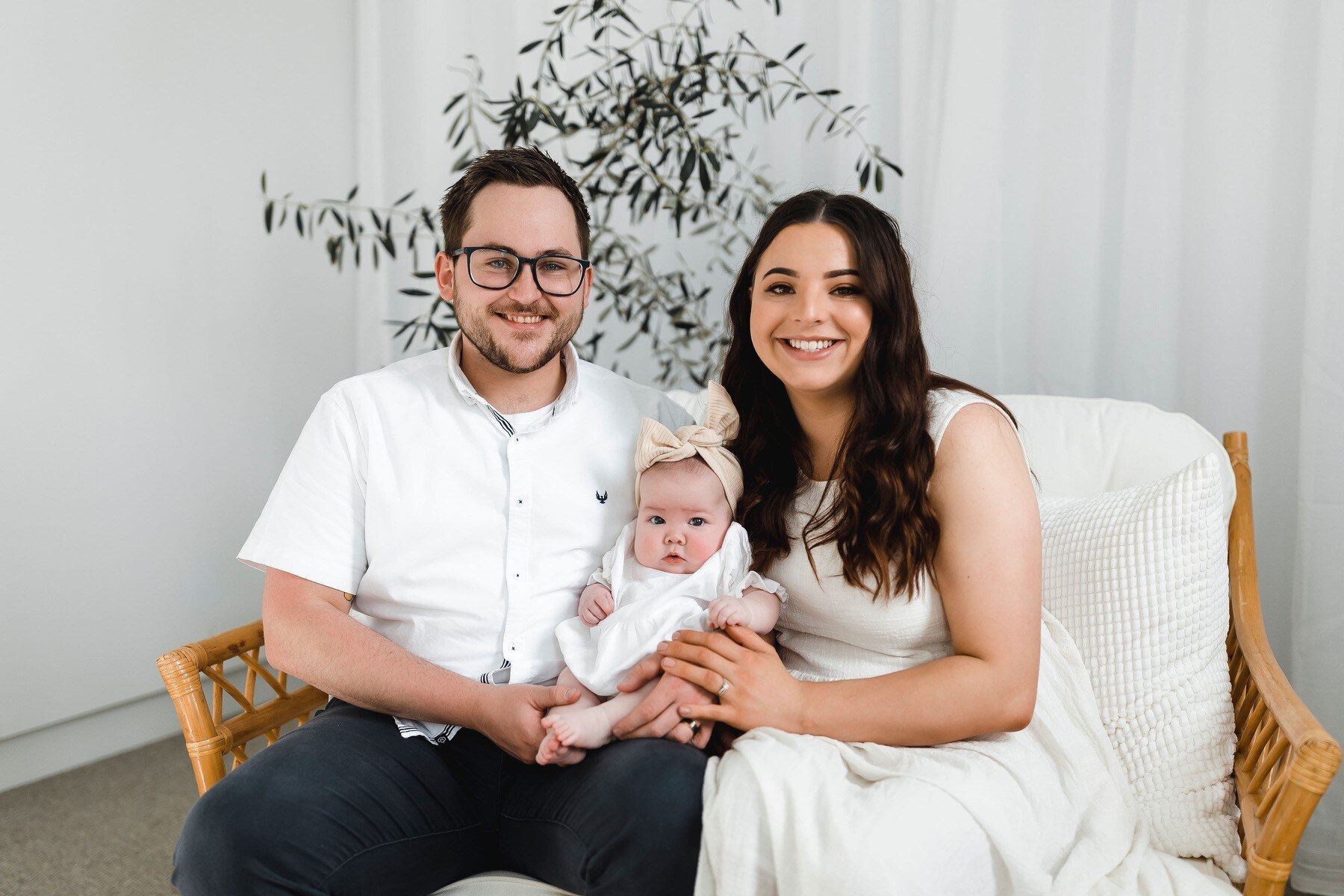 A man and woman smiling and holding a baby while sitting no a couch.