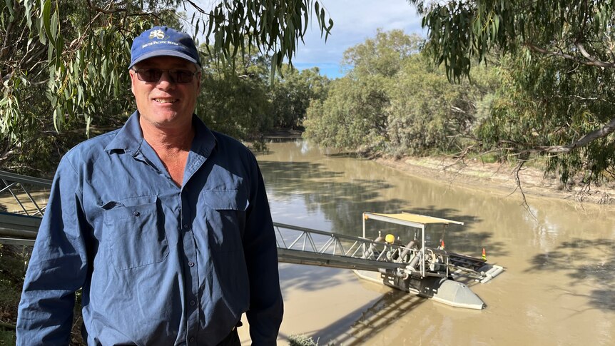 Andrew Rix stands on the river bank and in the background is his irrigation pump