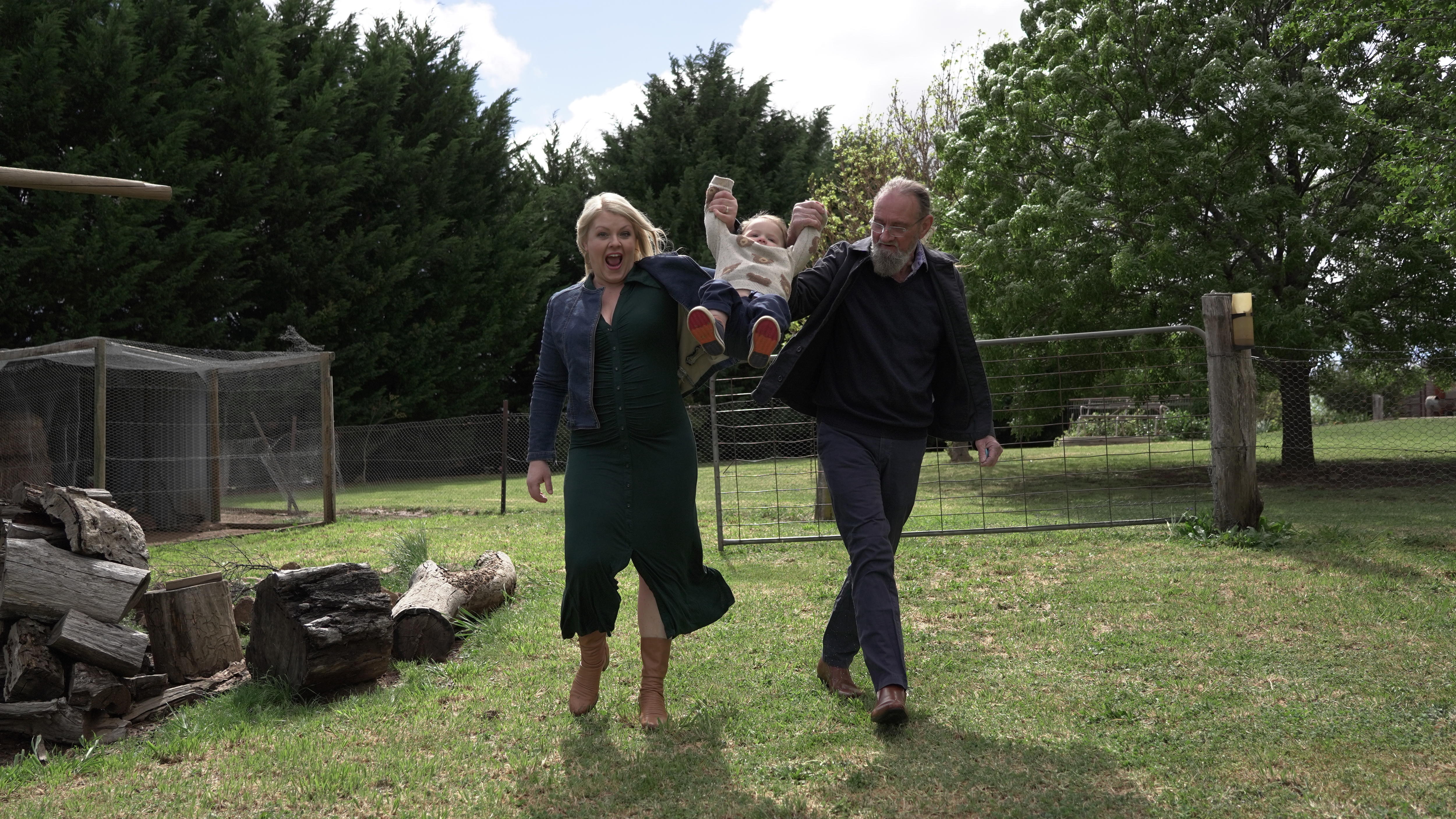 Catherine and Gregory walking on grass, each holding hands with baby William, swinging him in the air.