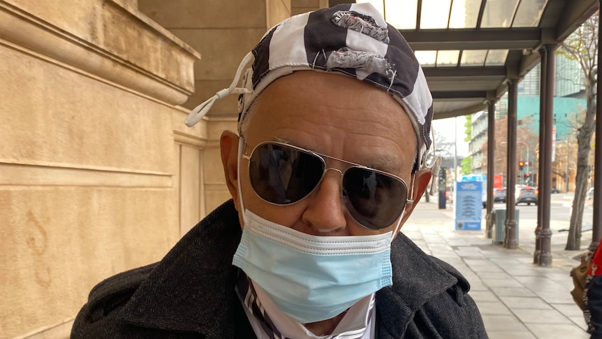 A man wearing a black and white hat and tie, a face mask and sunglasses