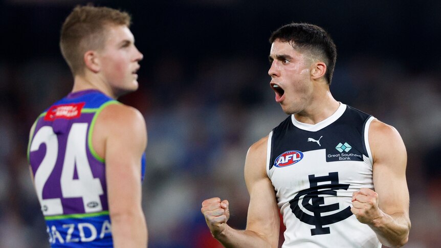 A Carlton player pumps his fist in celebration as a dejected Kangarooos defender looks down the ground. 