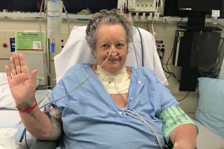 Una mujer sentada en una habitación de hospital con una bata quirúrgica con tubos que le corren por la nariz. 