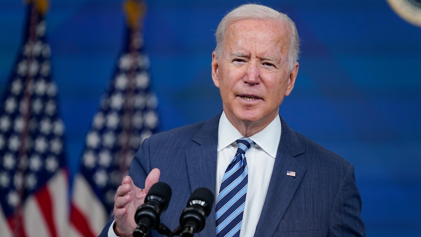 Joe Biden gestures as he speaks in front of two US flags