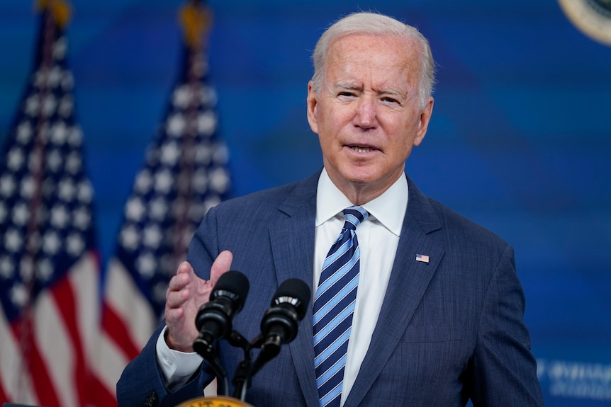 Joe Biden gestures as he speaks in front of two US flags