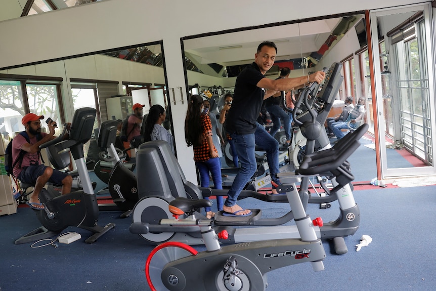 A man in thongs is mid-stride on a cross trainer surrounded by other gym equipment