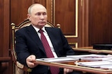 Vladimir Putin sits at a desk with a very ominous expression on his face.