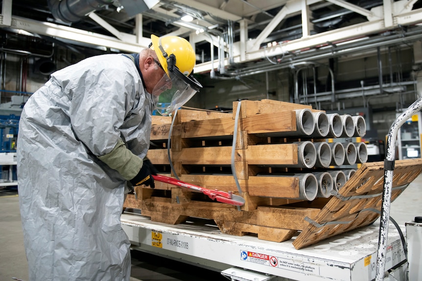An operator cuts the metal bands on a timber pallet of cylindrical grey rockets.