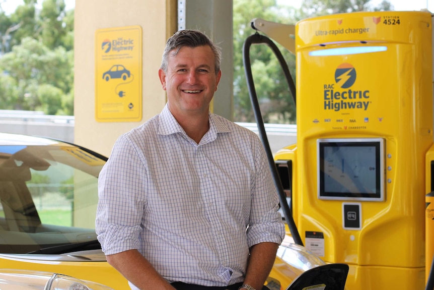 A mid-shot of a man standing next to an electric car charging station.