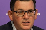 Premier Daniel Andrews, dressed in a shirt and jacket, delivers a press conference in front of a purple backdrop.