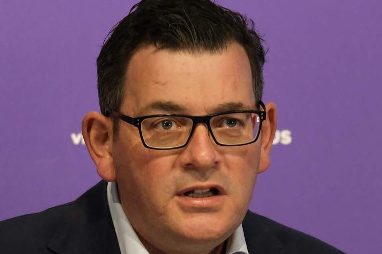 Premier Daniel Andrews, dressed in a shirt and jacket, delivers a press conference in front of a purple backdrop.