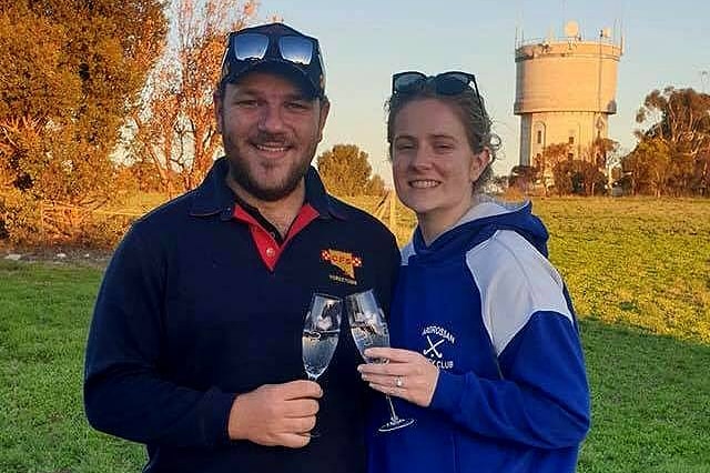 A man and a woman holding champagne flutes in front of a water tower