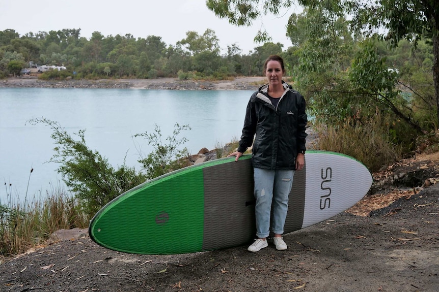 A woman stands with a paddle board