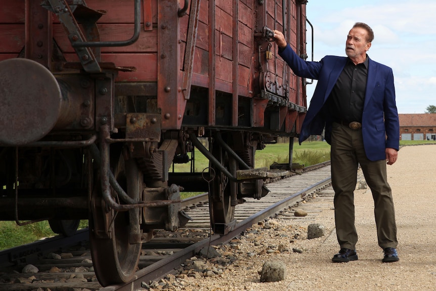 Arnold Schwarzenegger examines an old train carriage used to transport Jews to Auschwitz.