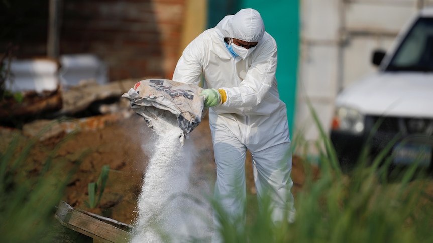 A forensic expert wearing white protective suit  throws lime on discarded protective equipment.