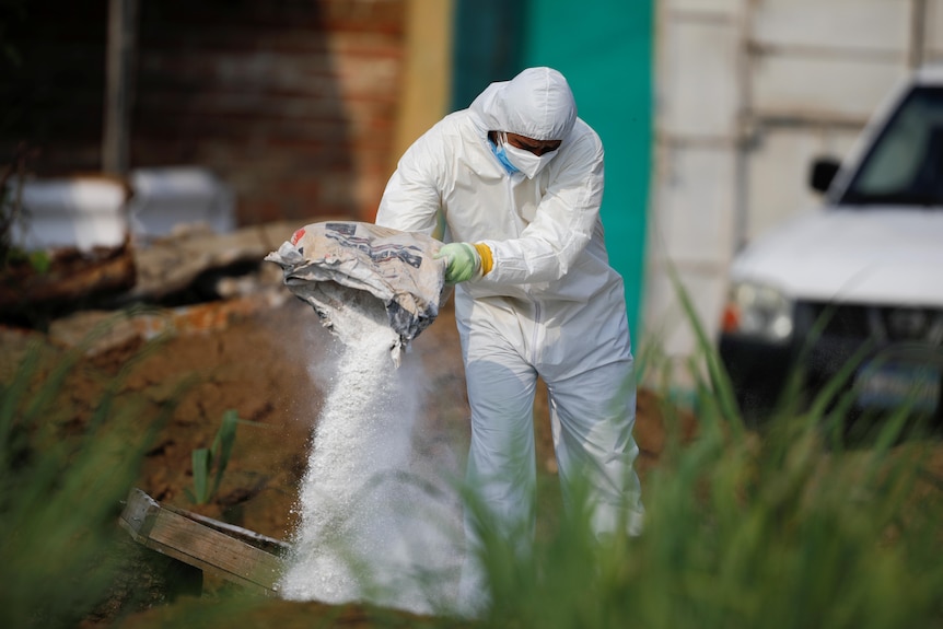 A forensic expert wearing white protective suit  throws lime on discarded protective equipment.