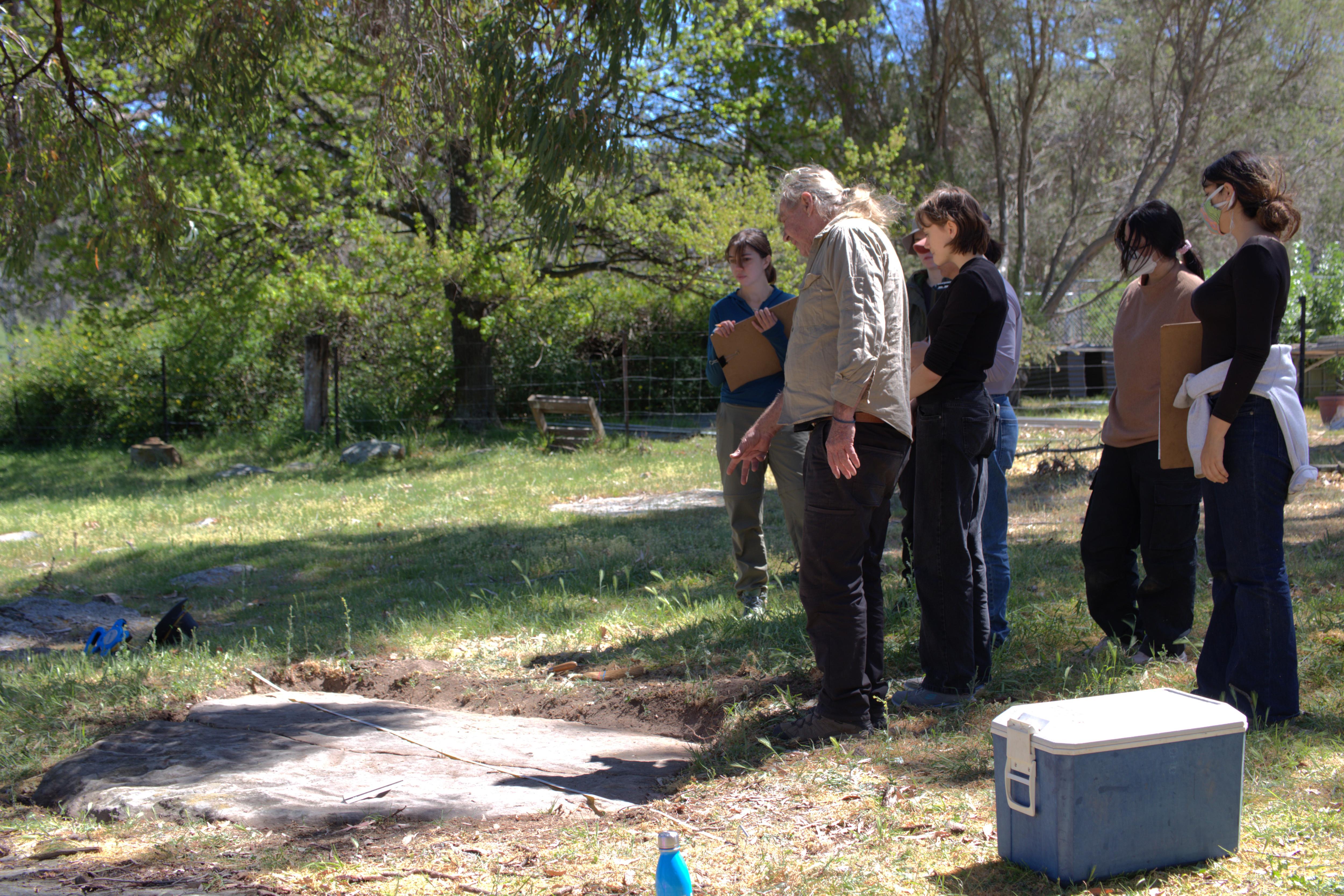 A man talking to students next to a rock formation