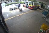 Paramedics in uniform lean into a white car while a man walks around it