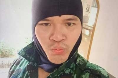A man in military fatigues purses his lips with a balaclava on and takes a selfie.