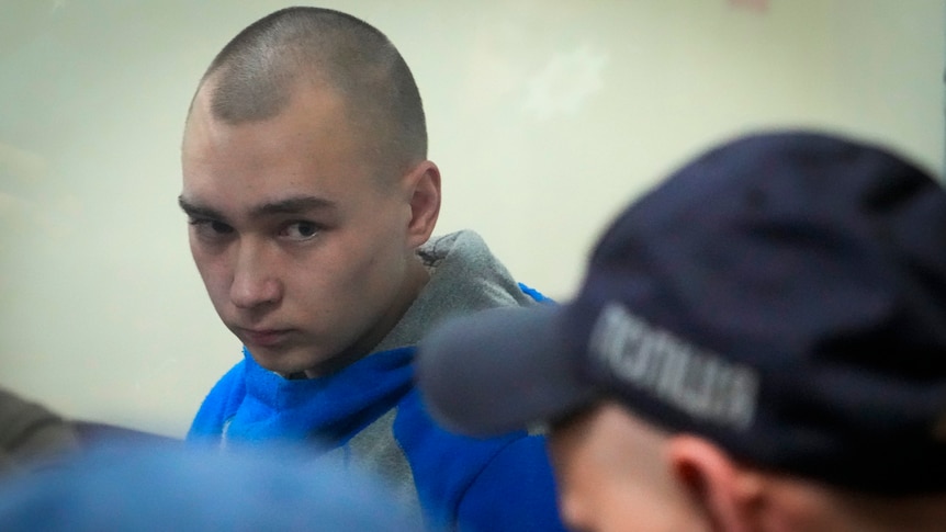 A young man with a shaved head looks towards a police officer