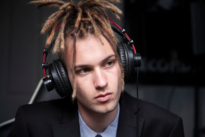 A young man wears headphones and looks into the middle distance