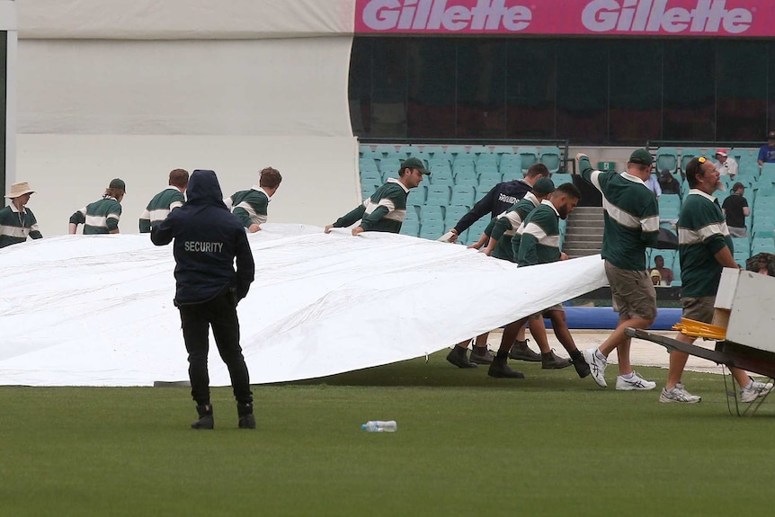 Ground crew pulls a tarpaulin over the pitch as rain falls at SCG on day five of the fourth Test.