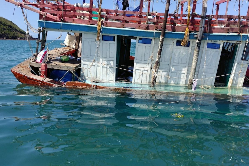 Close view of part of an older style boat with faded paint, listing to one side, with part of the deck underwater