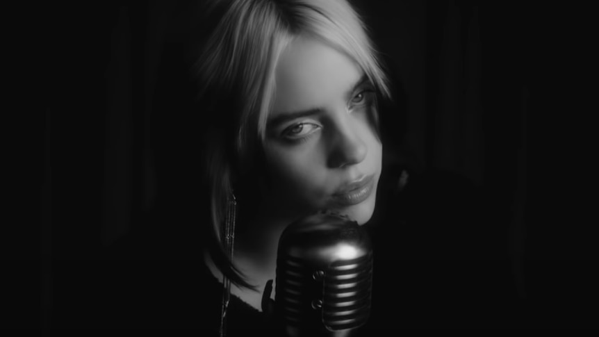 Screenshot of Billie Eilish, black and white, singing into microphone