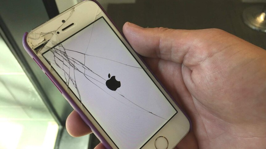 A man holds an Apple iPhone with a cracked screen.