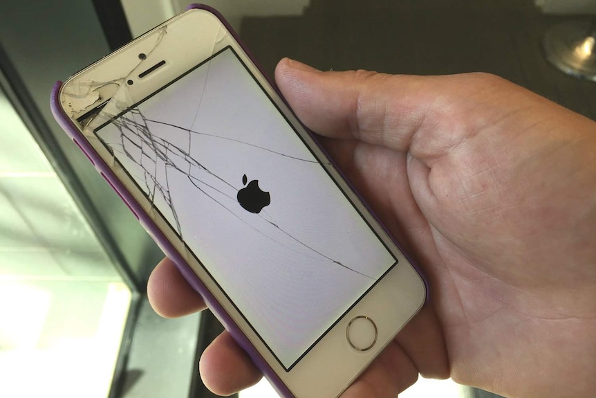 A man holds an Apple iPhone with a cracked screen.