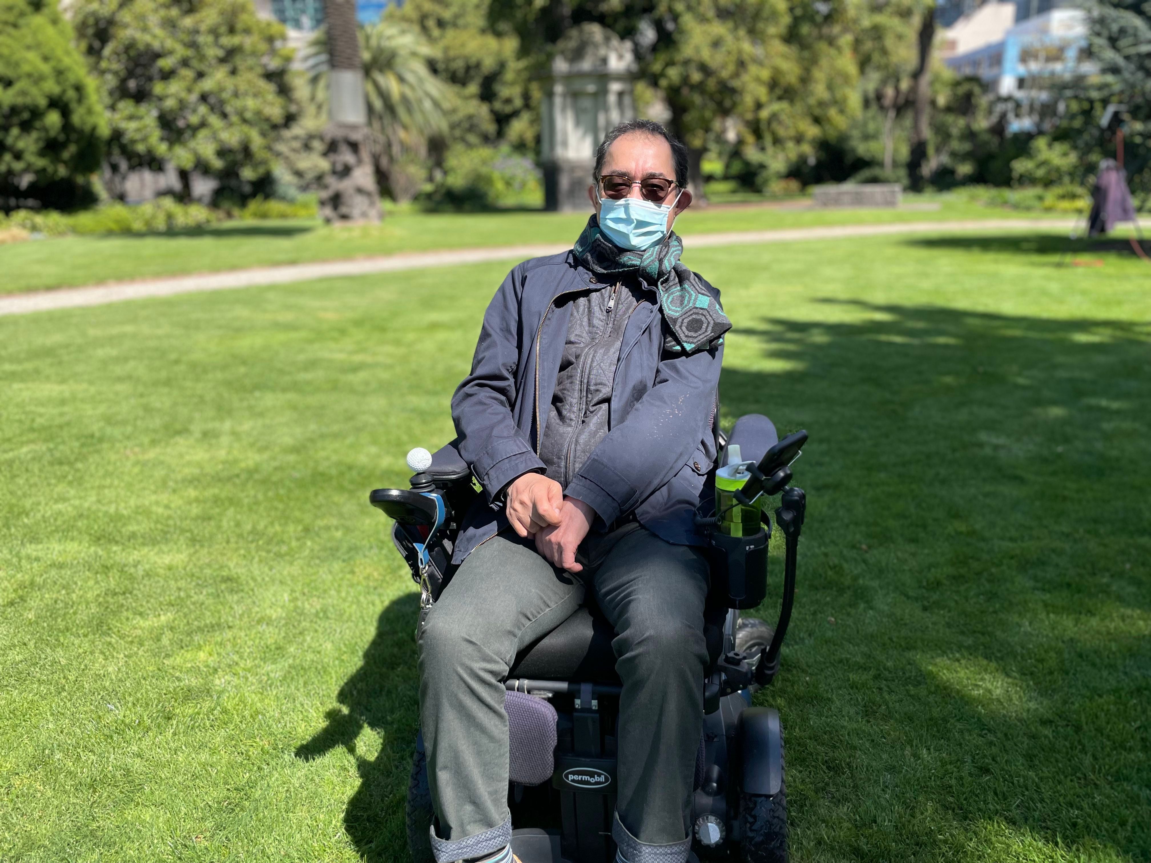 A man wearing sunglasses and mask sits in a wheelchair.