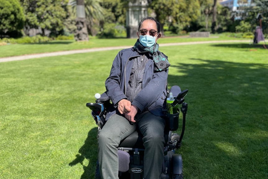 A man wearing sunglasses and mask is sitting in a wheelchair.