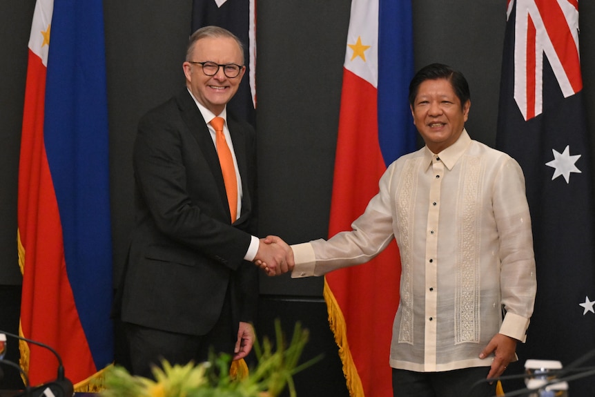 Anthony Albanese meets and Ferdinand R Marcos Jr stand side by side shaking hands in front of flags.